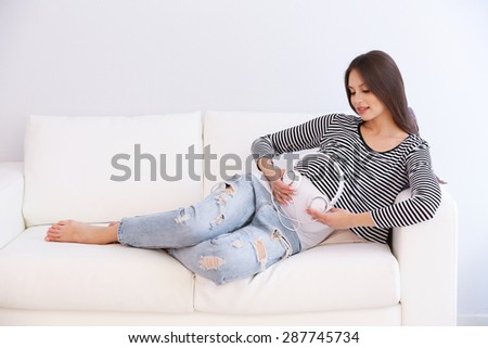 Pregnant woman with headphones on sofa in room