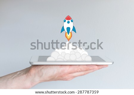 Concept of successful mobile computing business or strategy, e.g. for app development or business startups. Rocket launching from white and silver tablet or smart phone. Hand holding mobile device.