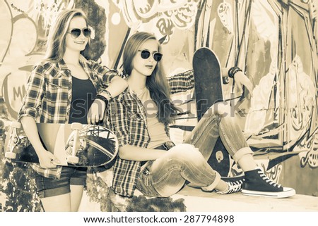 Vintage image of young beautiful girls with skateboard outdoors. Retro styled portrait of smiling teenagers near urban wall.