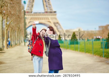Two cheerful beautiful girls in Paris doing self picture (selfie) using mobile phone near the Eiffel tower