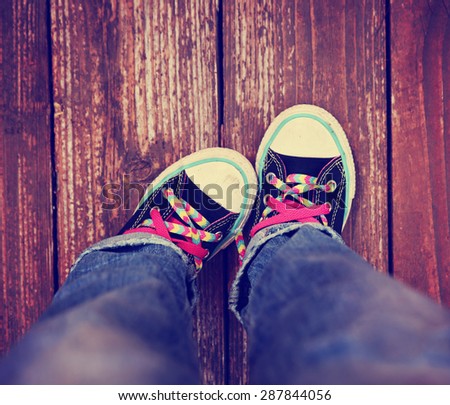 a wide angle photo of a pair shoes with pink shoe laces on a vintage wooden background pointing one toe in toned with a retro vintage instagram effect app 
