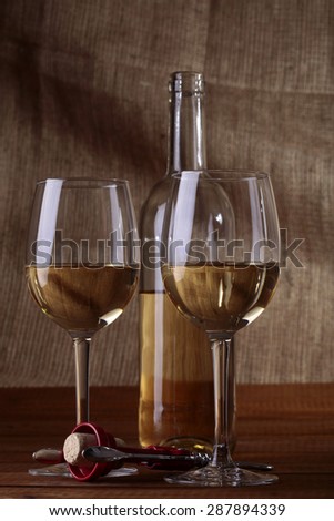 Two bocals and bottle of white wine with corkscrew on wooden table top on brown background, vertical picture