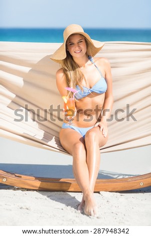 Pretty woman holding cocktail in the hammock at the beach