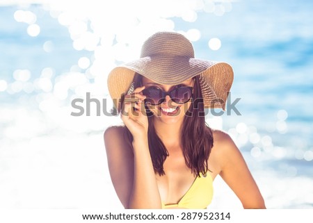 Brunette relaxing with a straw hat smiling at camera at the beach