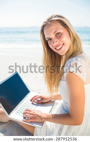 Woman using laptop and wearing hat on beach
