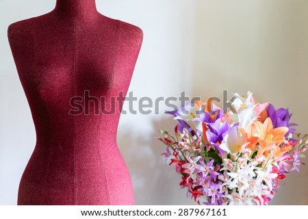Purple clothing mannequin with colorful flowers vase on white cement wall background