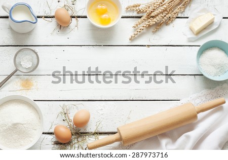 Baking cake in rustic kitchen - dough recipe ingredients (eggs, flour, milk, butter, sugar) on white planked wooden table from above. Background layout with free text space. Royalty-Free Stock Photo #287973716