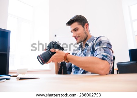 Casual happy young man sitting at the table with photo camera 