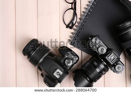 Modern cameras with glasses and notebook on wooden table, top view Royalty-Free Stock Photo #288064700