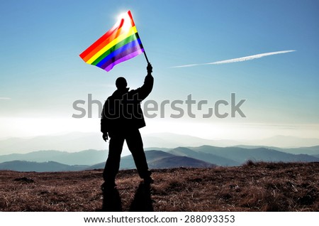 successful silhouette man winner waving Homosexual gay flag on top of the mountain peak