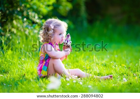 Child eating ice cream. Kids play outdoors enjoying sweet snack on a hot summer day. Children eat icecream. Toddler kid playing in the garden. Little girl with vanilla and chocolate ice cone.