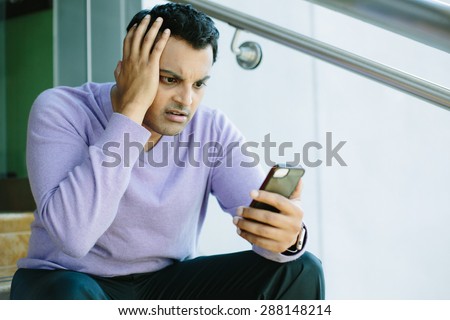 Closeup portrait, stressed young man in purple sweater, shocked surprised, horrified disturbed, by what he sees on his cell phone, isolated indoors background.