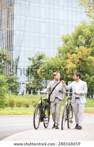 Businessmen talking while walking with bicycles on street Royalty-Free Stock Photo #288168659