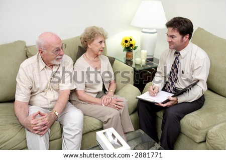 A marriage counselor or salesman meeting with a senior couple.  The wife is receptive but the husband looks skeptical