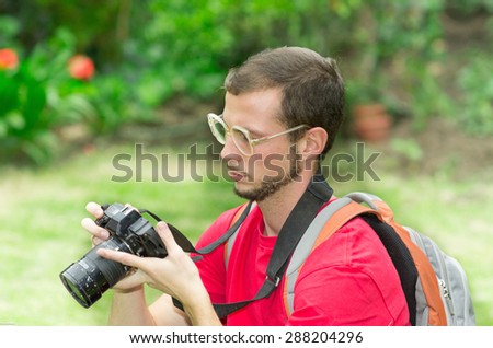 Man in red t-shirt taking looking at camera in the park with grassy background