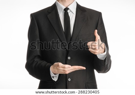 Businessman and gesture topic: a man in a black suit and tie with his left hand shows a thumbs up sign and holding his right hand on a white isolated background in studio