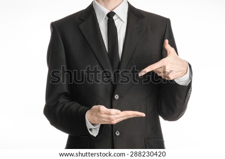 Businessman and gesture topic: a man in a black suit with a tie shows the left hand index finger on his right hand on a white isolated background in studio