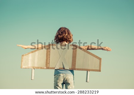 Happy child playing with toy wings against summer sky background. Retro toned Royalty-Free Stock Photo #288233219