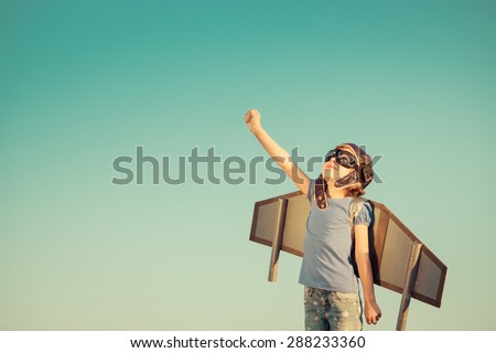 Happy child playing with toy wings against summer sky background. Retro toned Royalty-Free Stock Photo #288233360