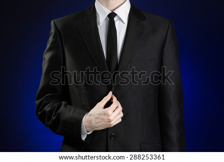 Businessman and gesture topic: a man in a black suit and white shirt correcting a jacket and tie on a dark blue background in studio isolated