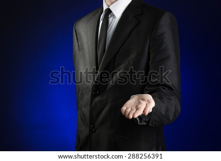 Businessman and gesture topic: a man in a black suit and white shirt holds up a hand against the dark blue isolated background in studio