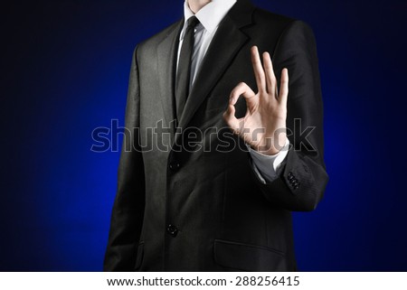 Businessman and gesture topic: a man in a black suit and white shirt showing okay hand sign on a dark blue background in studio isolated