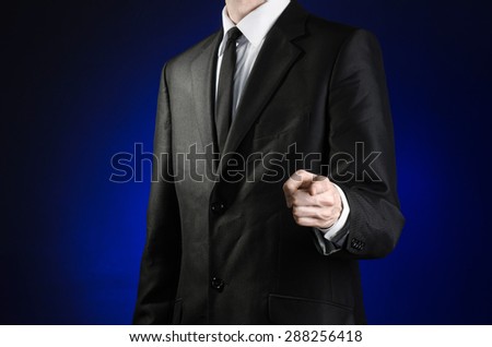 Businessman and gesture topic: a man in a black suit and white shirt shows his hand forward on a dark blue background in studio isolated
