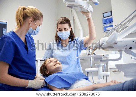 people, medicine, stomatology and health care concept - happy female dentist with assistant and patient girl at dental clinic office Royalty-Free Stock Photo #288278075