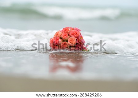 Bouquet of scarlet roses lying on sandy beach with surf closeup on water background, horizontal picture