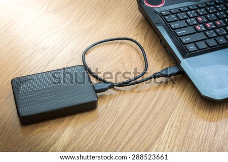 External hard drive connected to laptop on wooden background
