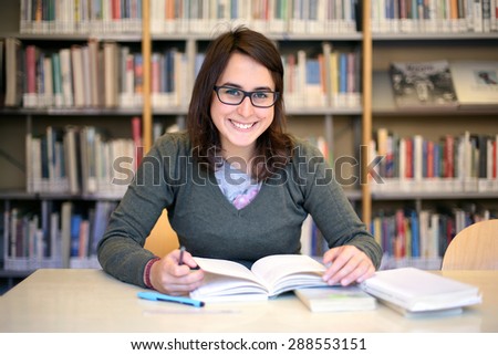 in the library - portrait of pretty female student with books while works and smiles 