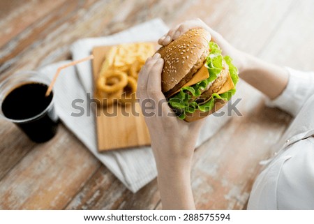 fast food, people and unhealthy eating concept - close up of woman hands holding hamburger or cheeseburger Royalty-Free Stock Photo #288575594