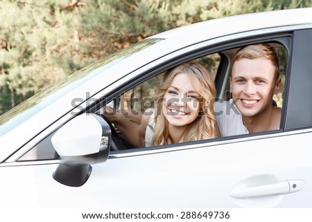 Lovely couple. Portrait of a young beautiful blond woman with curvy hair and her handsome boyfriend sitting in a car near to each other looking out of the window smiling happily