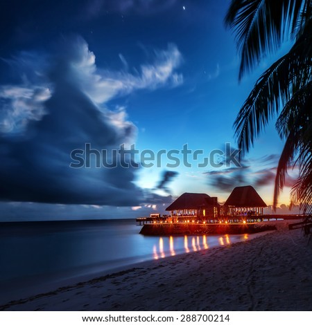 Paradise beach at night, glowing light in the restaurant over water, romantic place for honeymoon vacation, summer evening on exotic island, Maldives landscape Royalty-Free Stock Photo #288700214