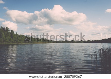 White clouds on the blue sky over blue lake with reflections - retro vintage film look
