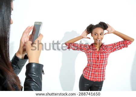 Looking funny. Pretty young girl holding her hands near her face and smiling while the friend making shots