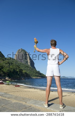 Young athletic man standing with sport torch facing the Rio de Janeiro Brazil skyline with Sugarloaf Mountain at Red Beach Urca