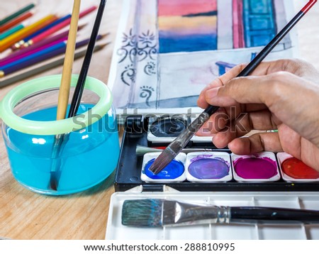 Hands holding brush with watercolor paints, architectural  sketchbook/ concept  for artist painting
