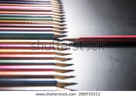 one red pencil standing out from the series of colorful pencils isolated on black background Sign symbol idea concept of leadership, opposition, confrontation Standoff of the individual to society