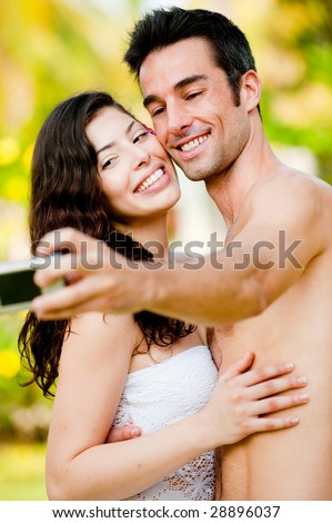 A young couple on vacation taking their photograph outside in tropical setting