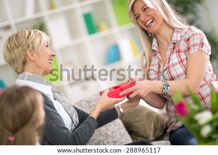 
Adult daughter giving to her mother gift for Mother's Day while little girl looking 