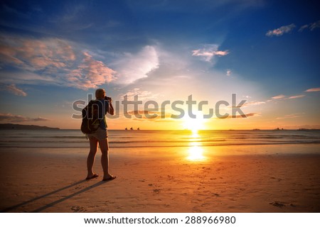 Photographer standing on beach  taking photo of beautiful sunset over sea 