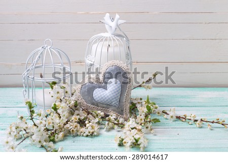 Background with white spring blossom  of trees, decorative heart  and candles in  bird cages on turquoise wooden planks.  Selective focus. Place for text. 