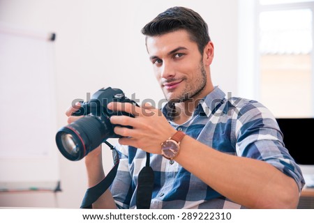 Happy man in casual cloth sitting at the table with photo camera