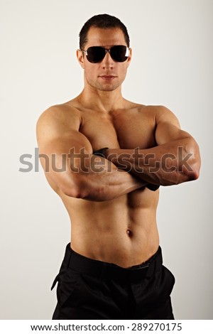 Muscular man in sunglasses standing on gray background