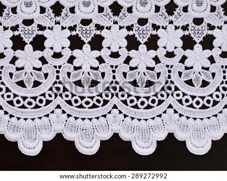 White openwork lace border on dark brown wooden background.