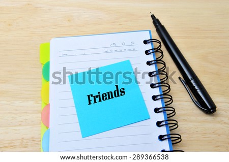 Friends words written on a blue sticky note pinned, notebook with pan on wooden background