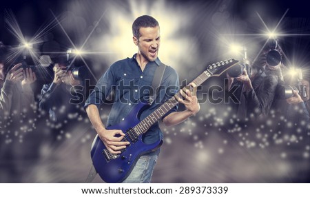 handsome young man playing electric guitar in front of photographers paparazzi