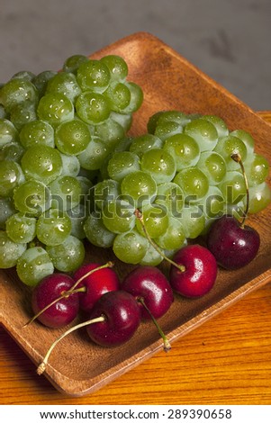 Many Variety fresh fruit(green grape, red cherry) on the wood tray, table in the grey background at the studio.