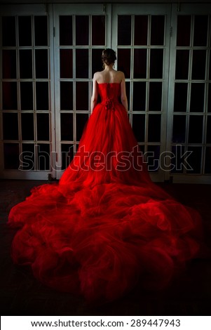 Beautiful girl in long red dress and in royal crown standing near retro fireplace door with stained-glass windows